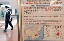 日本东京羽田机场一名戴着口罩的警察走过武汉肺炎的防疫广告牌。（2020年1月20日）