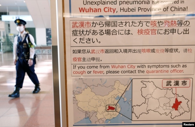 日本东京羽田机场一名戴着口罩的警察走过武汉肺炎的防疫广告牌。(2020年1月20日)