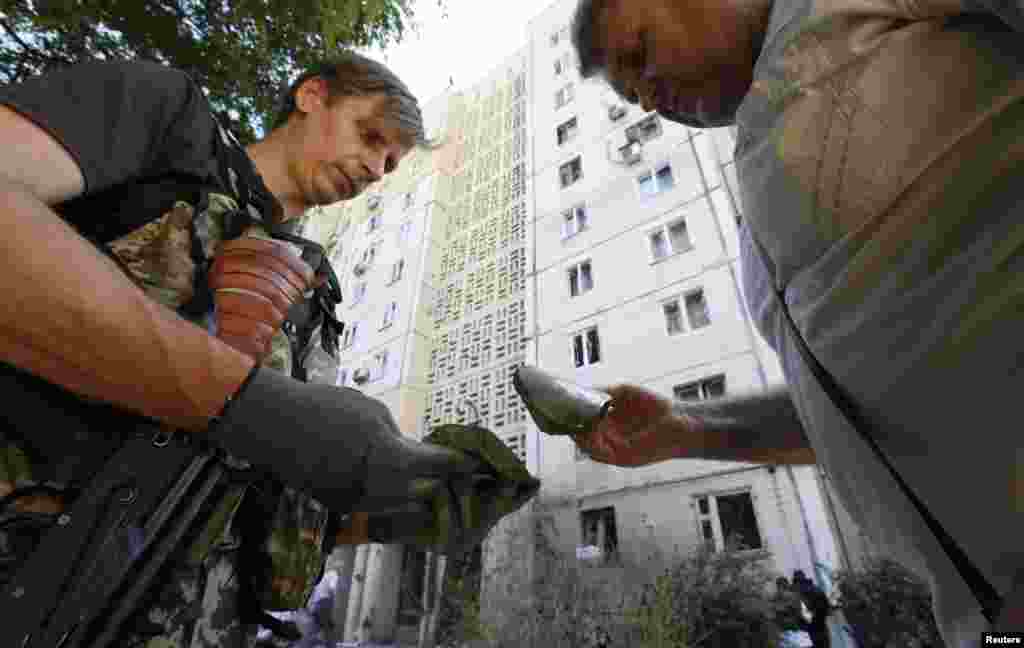 An armed pro-Russian separatist (left) and a man examine fragments of spent ammunition in central Donetsk, July 29, 2014.