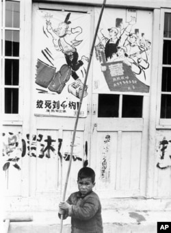 历史照片：在上海，一名男孩拿着竹竿在“绞死刘少奇”的宣传画前嬉戏。(1967年5月27日)