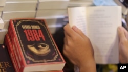 A person reads a book next to copies of British writer George Orwell's "1984." (Photo by Aaron Tam / AFP)