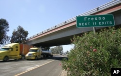 FILE - Trucks fly by a Fresno sign on California State Route 99, Aug. 23, 2011, in Fresno, Calif.