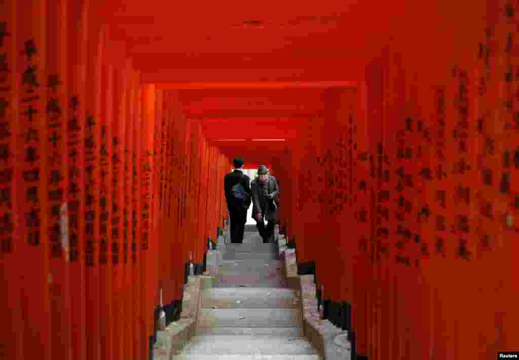 Visitors wearing protective face masks walk through red-colored wooden torii gates at a shrine in Tokyo, Japan.