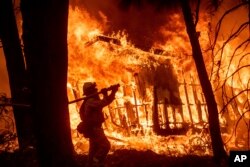 FILE - Firefighter Jose Corona sprays water as flames from the Camp Fire consume a home in Magalia, California, Nov. 9, 2018.