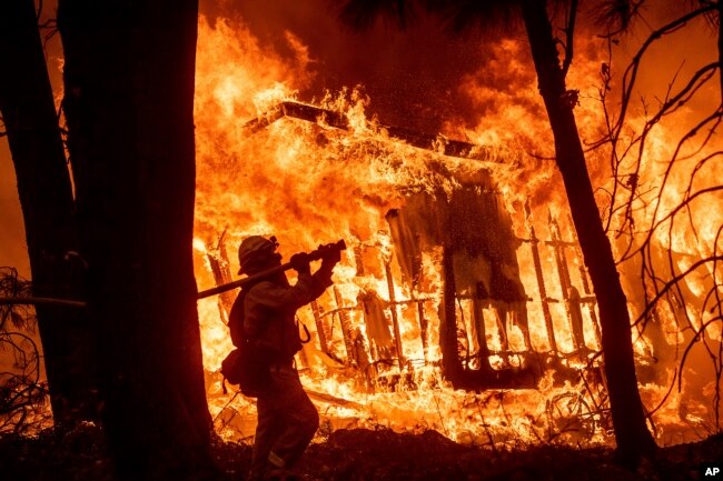 FILE - Firefighter Jose Corona sprays water as flames from the Camp Fire consume a home in Magalia, California, Nov. 9, 2018.