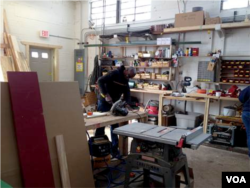 Paul Muthamia works in the shop building shelves, which helps him earn his house. (Noah Phillips/VOA)