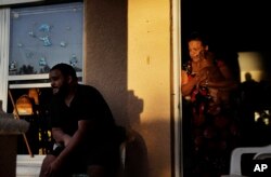 FILE - Sandra Pagan, right, looks out from her front door while escaping the heat inside her home with her dog Goldo, nephew Misael Fernandez, center, and niece Lorraene Andaluz, in window at left, after Hurricane Irma flooded their neighborhood leaving them without power and impassable with their cars in Fort Myers, Fla., Sept. 12, 2017. "It's unbearable," said Pagan.