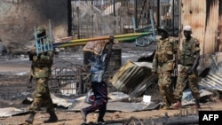 A Sudanese man carries a bed past South Sudan People's Liberation Army (SPLA) soldiers patrolling Bentiu early on in South Sudan's conflict. Fighting broke out again in the town in October 2014. 