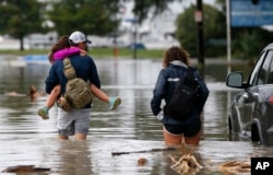 Don Noel carries his daughter Alexis, 8, with his wife Lauren, (right) as they walk through a flooded roadway in the West End section of New Orleans, June 21, 2017.