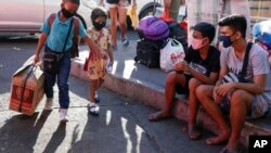 A young boy and girl hold hands as they arrive with their parents to try to catch a ride at the Cubao bus terminal in Manila, Philippines on Friday, March 13, 2020. Many people adjusted their travel plans ahead of a government suspension of domestic trave