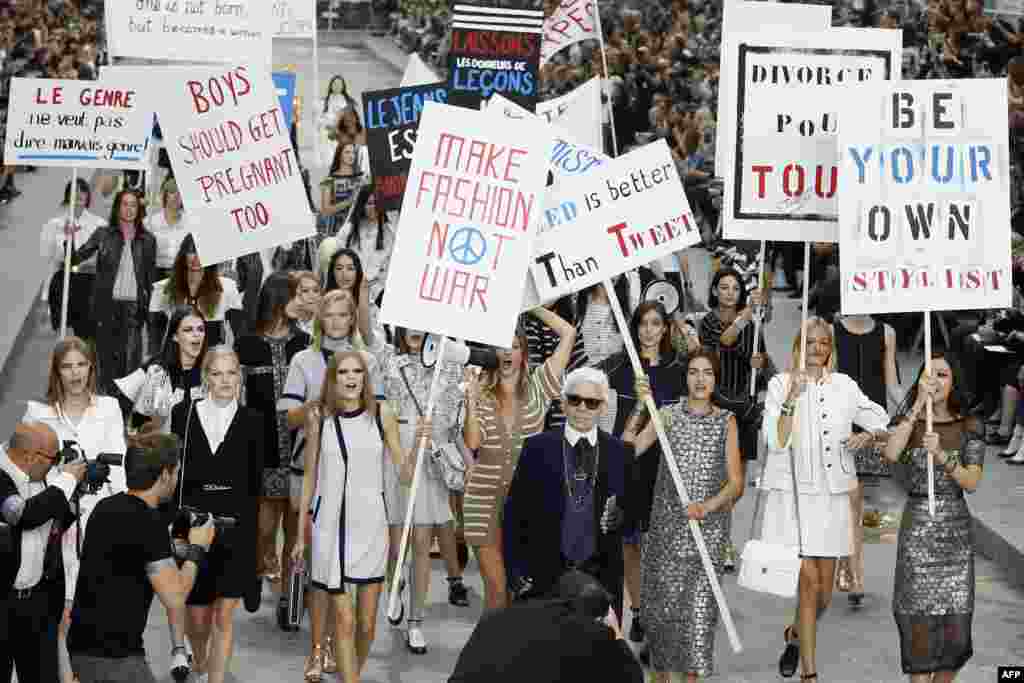 German fashion designer Karl Lagerfeld (C) acknowledges the public as Brazilian model Gisele Bundchen (back-C) speaks through a megaphone while she and other models fake a demonstration as they present creations for Chanel 2015 Spring/Summer ready-to-wear collection fashion show at the Grand Palais in Paris, France.