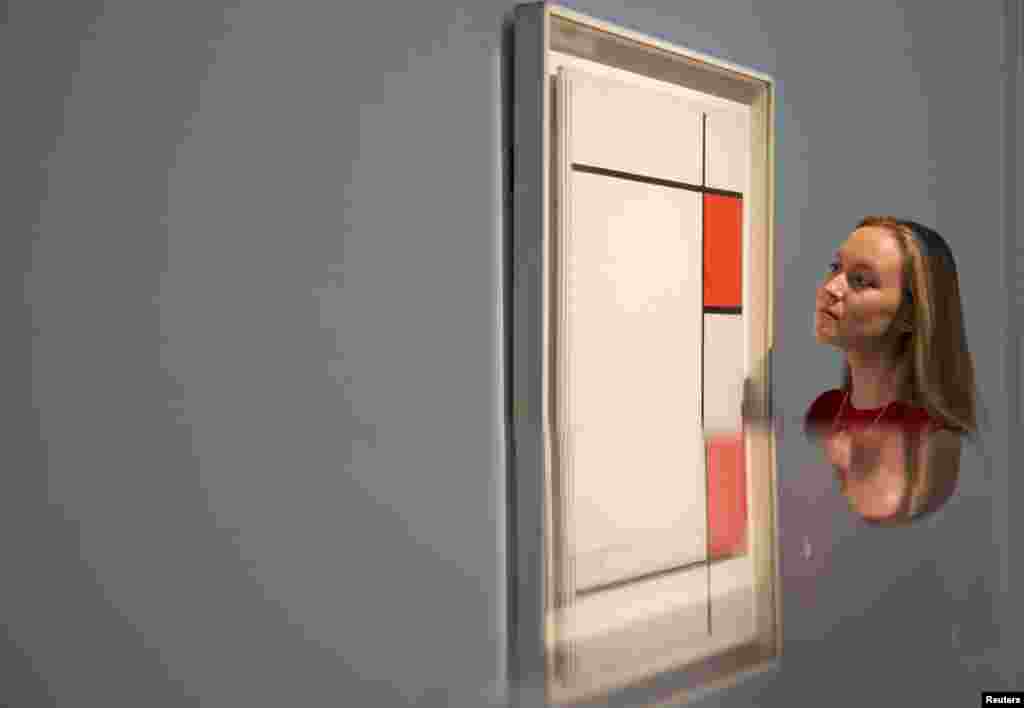 A gallery assistant is reflected as she views the work Composition with Red, Blue and Grey by Piet Mondrian during a photo-call for Impressionist and Modern Art Evening Sale at Sotheby's auction house in London.