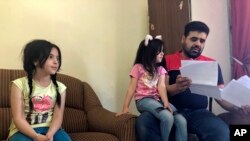 Keluarga pengungsi Suriah Mahmoud Mansour, dan putrinya Sahar dan Ruba, memegang dokumen permohonan pemukiman kembali di AS di apartemen sewaannya di Amman, Yordania, 27 Juni 2018. 