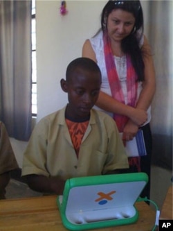 A Rwandan girl uses her new OLPC laptop while an onsite specialist looks on.