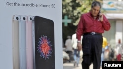 A man speaks on his mobile phone as he walks past an Apple iPhone SE advertisement billboard in a street in New Delhi, India, April 25, 2016.