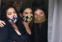 In this Monday, May 18, 2020, photo, Anissa Archuleta, center, sits at a window with her sister Alexis Archuleta, right, and her mother, Jaime Ortega, at their home in Midvale, Utah. The women all tested negative, but received daily calls from health investigators.