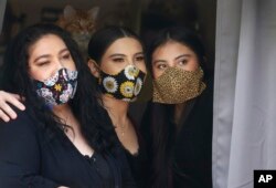 In this Monday, May 18, 2020, photo, Anissa Archuleta, center, sits at a window with her sister Alexis Archuleta, right, and her mother, Jaime Ortega, at their home in Midvale, Utah. The women all tested negative, but received daily calls from health investigators.