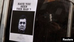 FILE -- A man takes photos of a "Wanted" notice, of fugitive Ukrainian President Victor Yanukovich, plastered on the window of a car used as barricade near Kyiv's Independent Square. 