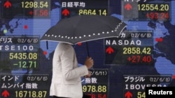 Seorang wanita melintasi layar elektronik yang menunjukkan kenaikan harga saham dunia di lantai bursa Tokyo (11/6).