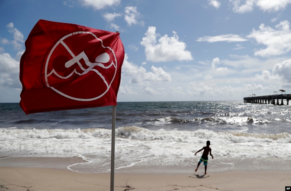 Un niño juega en la playa de Lake Worth, Florida, delante de una bandera que advierte a los bañistas no nadar a causa del oleaje causado por la cercanía del huracán Dorian, el sábado 31 de agosto de 2019. Dorian está azotando el noroeste de Bahamas como una tormenta de categoría 4. Los meteorólogos dicen que se espera que suba por la costa sureste de EE.UU., afectando además de Florida los estados de Georgia y las Carolinas. (Foto AP / Lynne Sladky)