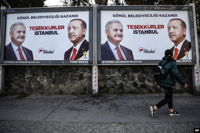 FILE - A woman walks past posters showing Binali Yildirim, left, the mayoral candidate for Istanbul of Turkey's President Recep Tayyip Erdogan's ruling Justice and Development Party's (AKP) a day after the local elections in Istanbul, April 1, 2019.