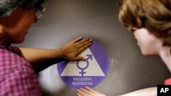 FILE - A new sticker is placed on the door at the ceremonial opening of a gender neutral bathroom at Nathan Hale high school in Seattle, May 17, 2016.