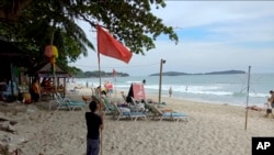 Un hombre levanta una bandera roja que indica condiciones meteorológicas adversas en la playa de Chaweng, Koh Samui, Tailandia, el jueves.