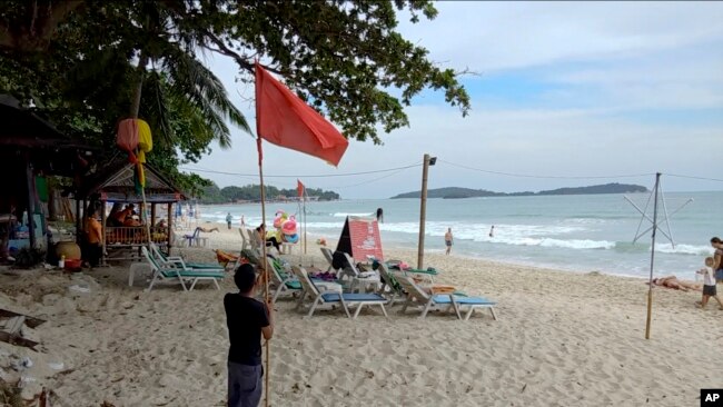 Un hombre levanta una bandera roja que indica condiciones meteorológicas adversas en la playa de Chaweng, Koh Samui, Tailandia, el jueves.