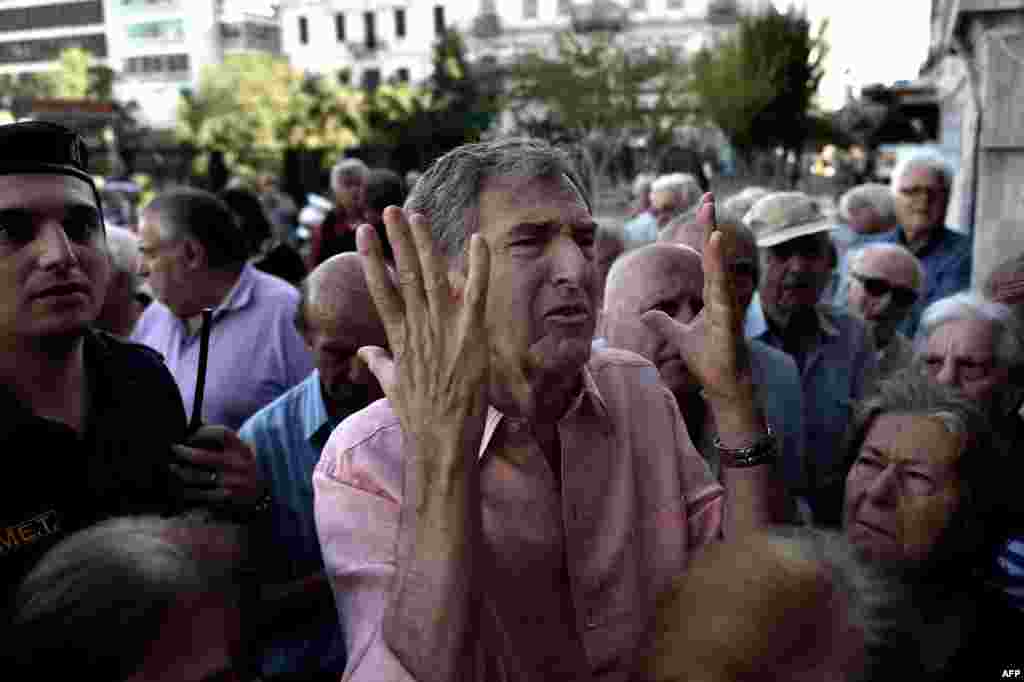 A man gestures as pensioners queue outside a national Bank branch where they cash out up to 120 euros, in Athens, Greece. The European Union will decide whether to grant Greece a last-minute bailout package to avoid pushing it further towards an exit from the eurozone.
