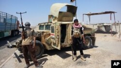Al-Qaida inspired militants stand with a captured Iraqi army Humvee at a checkpoint outside Beiji refinery, north of Baghdad, Iraq, June 19, 2014.