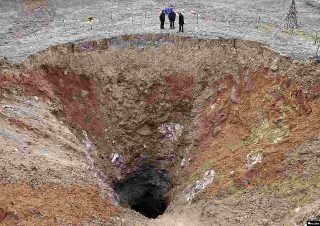 People stand next to a 24.9-meter (82 feet) diameter pit at a village in Guangyuan, Sichuan province, China, Feb. 28, 2013. The investigators said the pit may face further sinking after rains due to its geological conditions. 