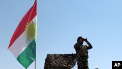 FILE - A member of the Kurdish security forces scans the horizon in Kirkuk, Iraq, from atop a military vehicle flying a flag of the Kurdistan Regional Government, June 14, 2014.