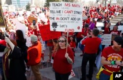 FILE - Amber Malin, a teacher in the Aurora, Colorado, public schools system, holds up a placard during a teacher rally in Denver, April 27, 2018.