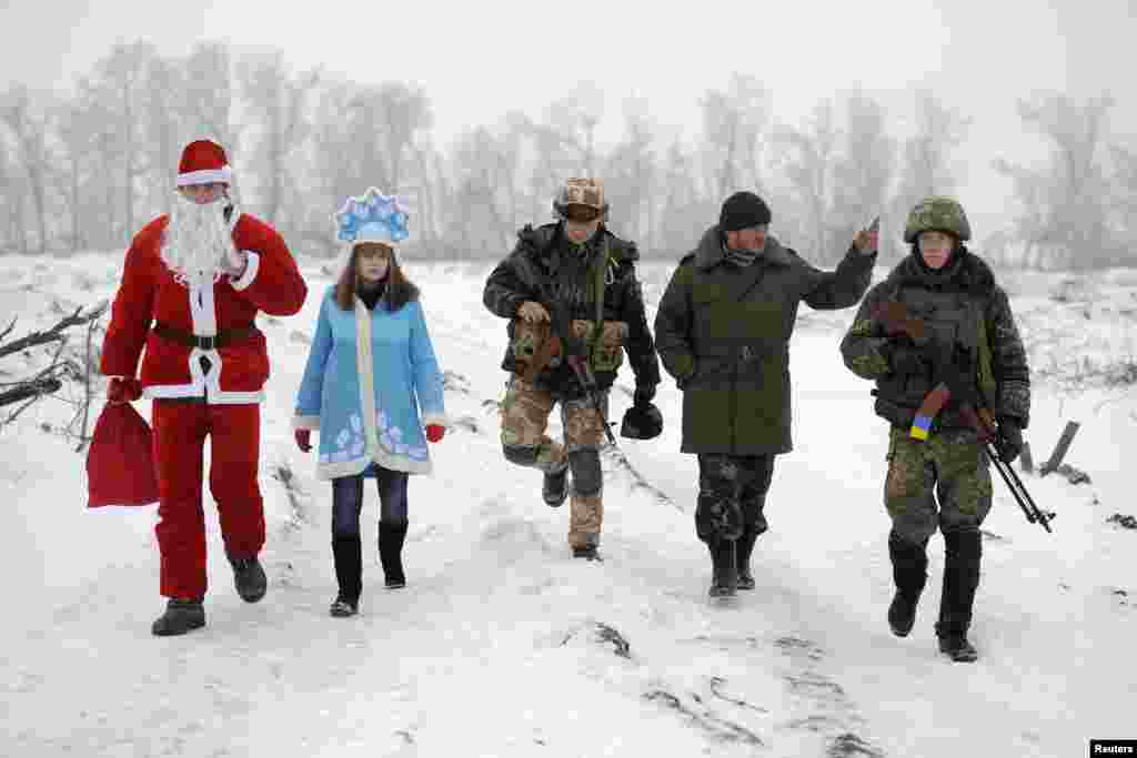 Penduduk lokal yang yang mengenakan kostum Bapak Salju, setara dengan Santa Klaus dan cucunya yang mengenakan kostum Snegurochka (Gadis Salju), berjalan dengan para tentara&nbsp; dan mengunjungi pos-pos pemeriksaan unit Angkatan Darat dan&nbsp; pertahanan Ukraina untuk mengucapkan selamat tahun baru kepada para militer, dekat Lysychansk, di Luhansk. &nbsp;