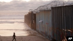 A woman walks on the beach, Jan. 9, 2019, next to the border wall topped with razor wire in Tijuana, Mexico.
