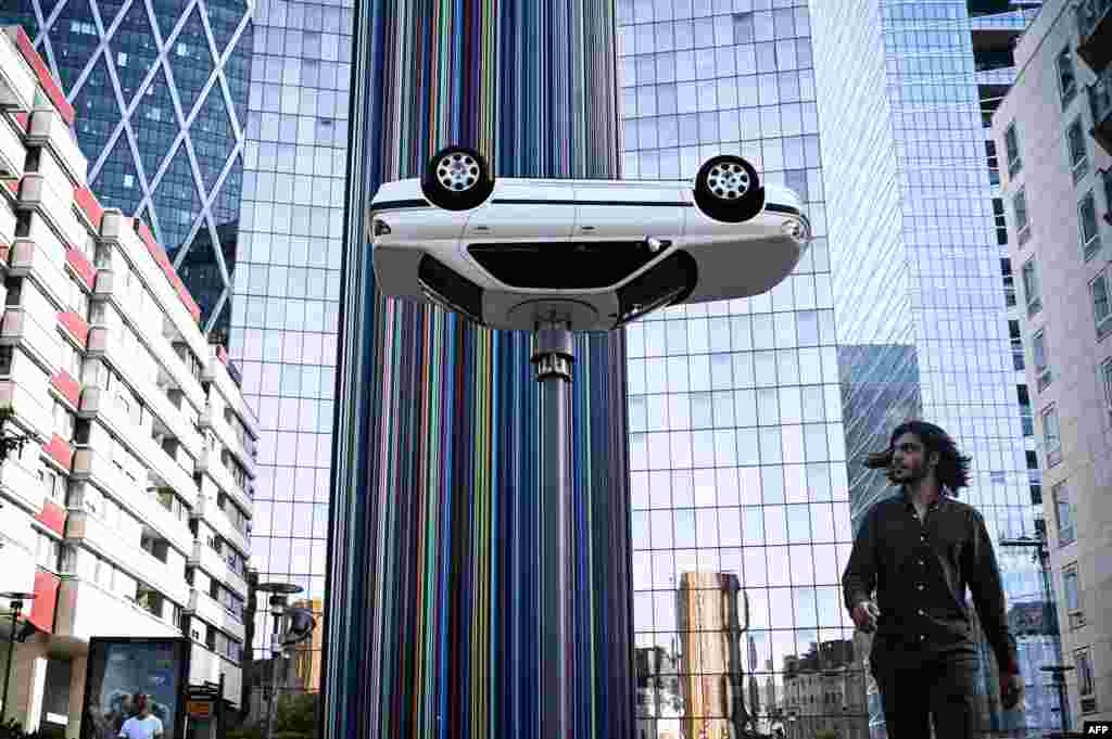 A man walks past an art installation by Benedetto Bufalino entitled 'La voiture sur le lampadaire' (the car on the lamp post), during "Les Extatiques," an open-air contemporary art exhibition in the business district of La Defense in Nanterre, west of Paris, France.