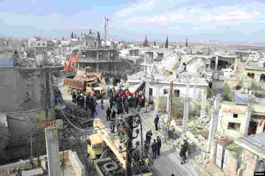 Bystanders look on as crews begin clearing the wreckage of a car bomb that exploded near a school in Al-Kafat, Syria, Jan. 9, 2014.