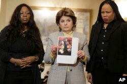 FILE - Latresa Scaff, right, and Rochelle Washington, left, look on as attorney Gloria Allred holds up a picture of them as teenagers on the night they claim they became victims of musician R. Kelly's sexual advances during a news conference in New York, Feb. 21, 2019.