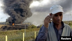 Un homme écoute sa radio près d’une colonne de fume à Skikda, dans l’est de l’Algérie, 6 octobre 2005.