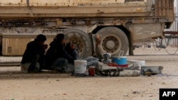 Displaced Syrians fleeing areas in the northern embattled province of Aleppo sit under a truck at the Bab al-Salama camp, set up outside the Syrian city of Azaz on Syria's northern border with Turkey, Feb. 12, 2016.