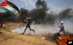 FILE - Palestinian protesters take cover from tear gas fired by Israeli troops after they burn tires near the fence during a protest at the Gaza Strip's border with Israel, east of Khan Younis, April 27, 2018.