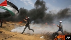 Palestinian protesters run to cover from tear gas fired by Israeli troops after they burn tires near the fence during a protest at the Gaza Strip's border with Israel, east of Khan Younis, April 27, 2018. 