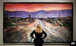 A woman looks towards a painting by Bob Dylan called "Endless Highway" on display at the exhibition called Bob Dylan The Beaten Path, at the Halcyon Gallery in London, Nov. 1, 2016.