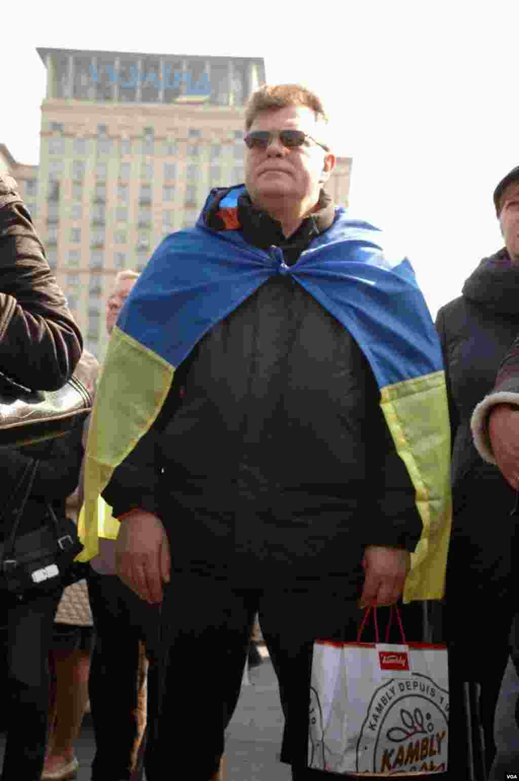 Un hombre arropado con la bandera de Ucrania escucha los discursos. (Steve Herman/VOA)