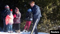 A Royal Canadian Mounted Police officer assists a child from a family that claimed to be from Sudan as they walk across the U.S.-Canada border into Hemmingford, Canada, from Champlain, New York, Feb. 17, 2017. (REUTERS/Christinne Muschi)