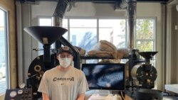 Carson Clough, co-founder of Giddy Goat Coffee Roasters, poses in front of the two roasting machines which processes fresh coffee daily inside the café. (VOA/Salim Fayeq)