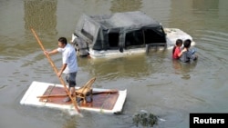 A man (L) paddles a makeshift raft as residents walks past a partially submerged car on a flooded street in Yuyao, Zhejiang province, Oct.11, 2013. 