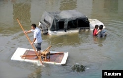 A man (L) paddles a makeshift raft as residents walks past a partially submerged car on a flooded street in Yuyao, Zhejiang province, Oct.11, 2013.
