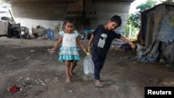 Children carry a drinking water container after filling it from a municipal tap under a flyover at a slum area in Kolkata, India, May 26, 2016. 