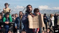 Des migrants protestent face aux barbelés qui séparent la Grèce de la Macédoine, samedi 27 février 2016. (AP Photo/Petros Giannakouris)